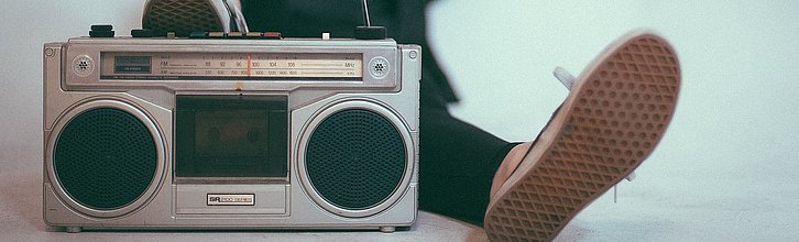 Ein Radio im Vordergrund, im Hintergrund liegt eine junge Person entspannt auf dem Boden