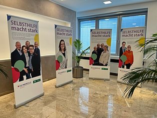 vier Roll-Ups nebeneinander mit Fotos von Selbsthilfegruppenmitgliedern